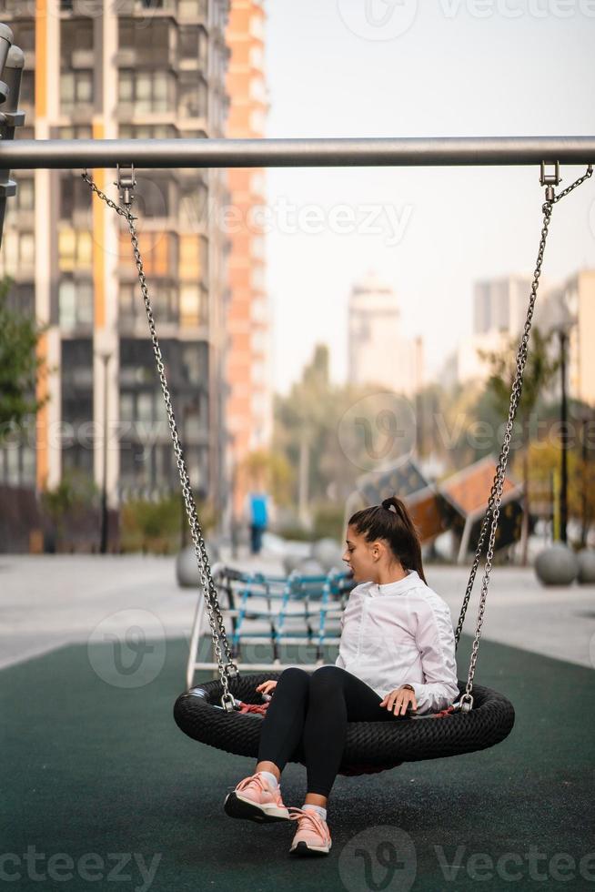 jong vrouw ritten Aan een schommel Bij de speelplaats. foto