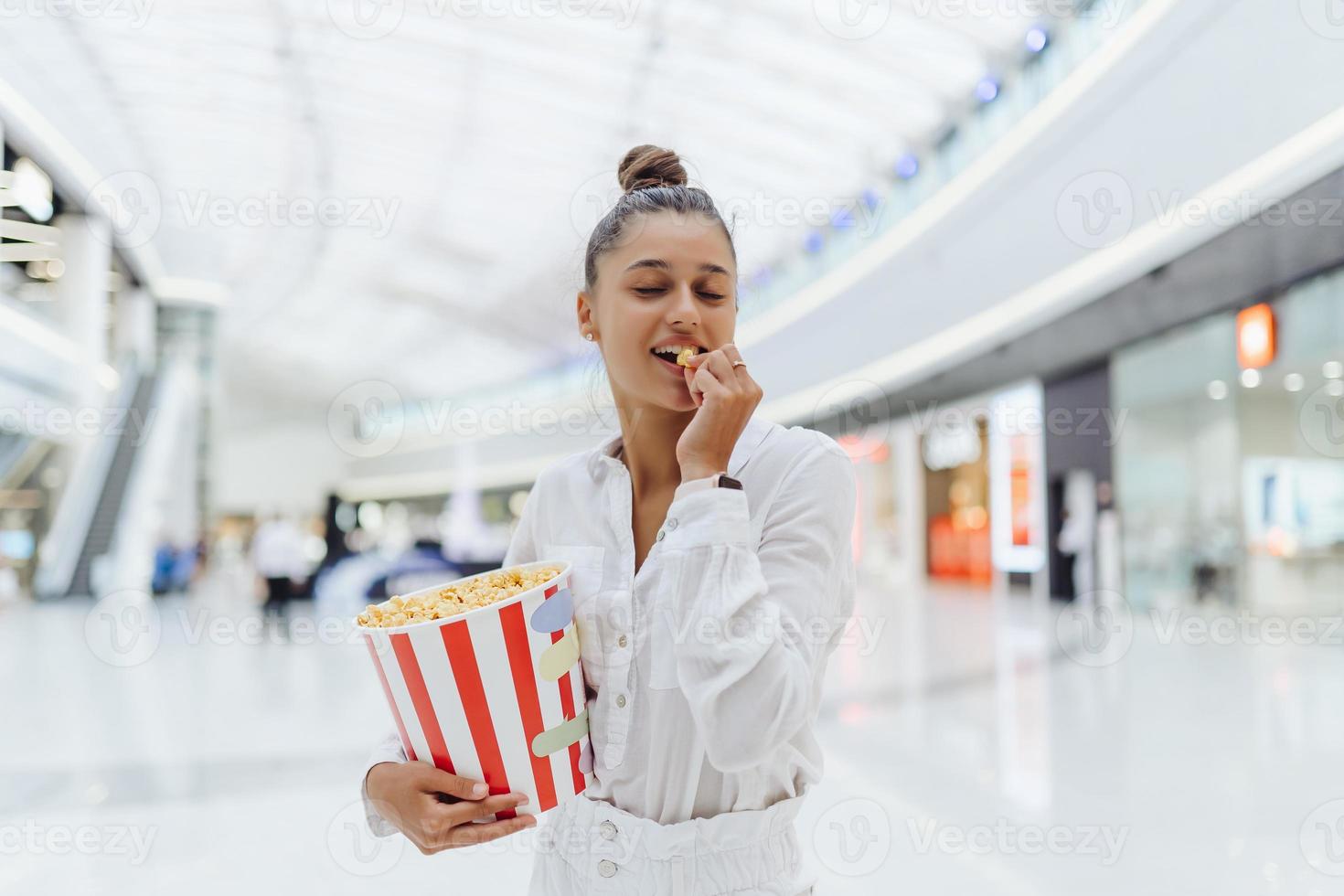jong schattig vrouw Holding popcorn in de winkelcentrum achtergrond foto