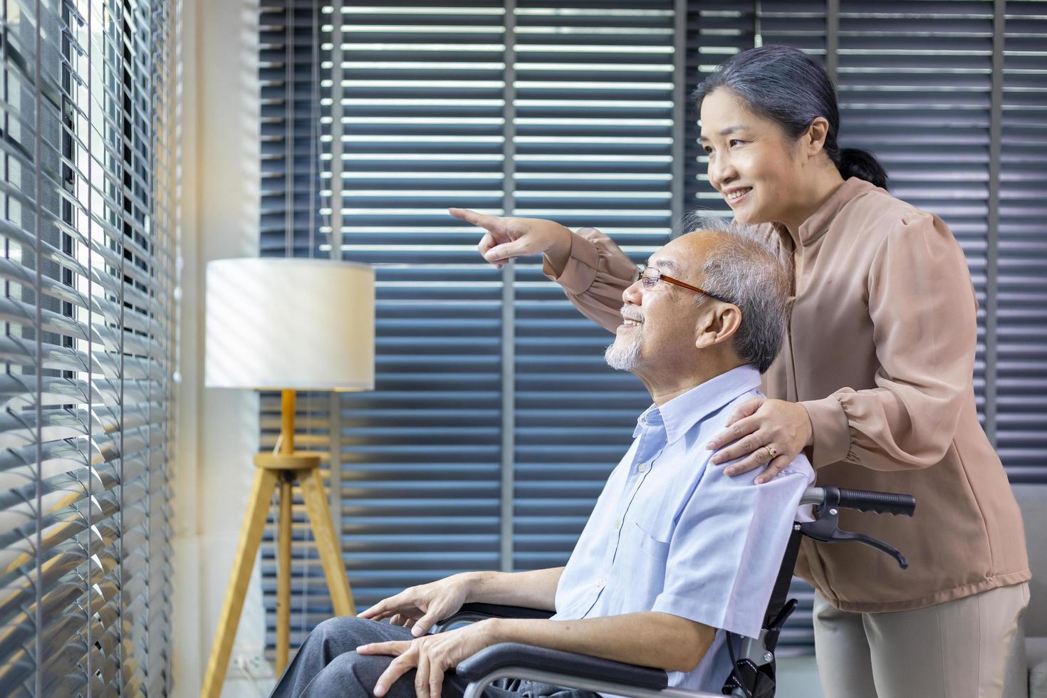 Aziatisch senior Mens zittend in rolstoel Bij huis met zijn vrouw is ondersteunen en zorgzaam voor liefde en pensioen familie concept foto