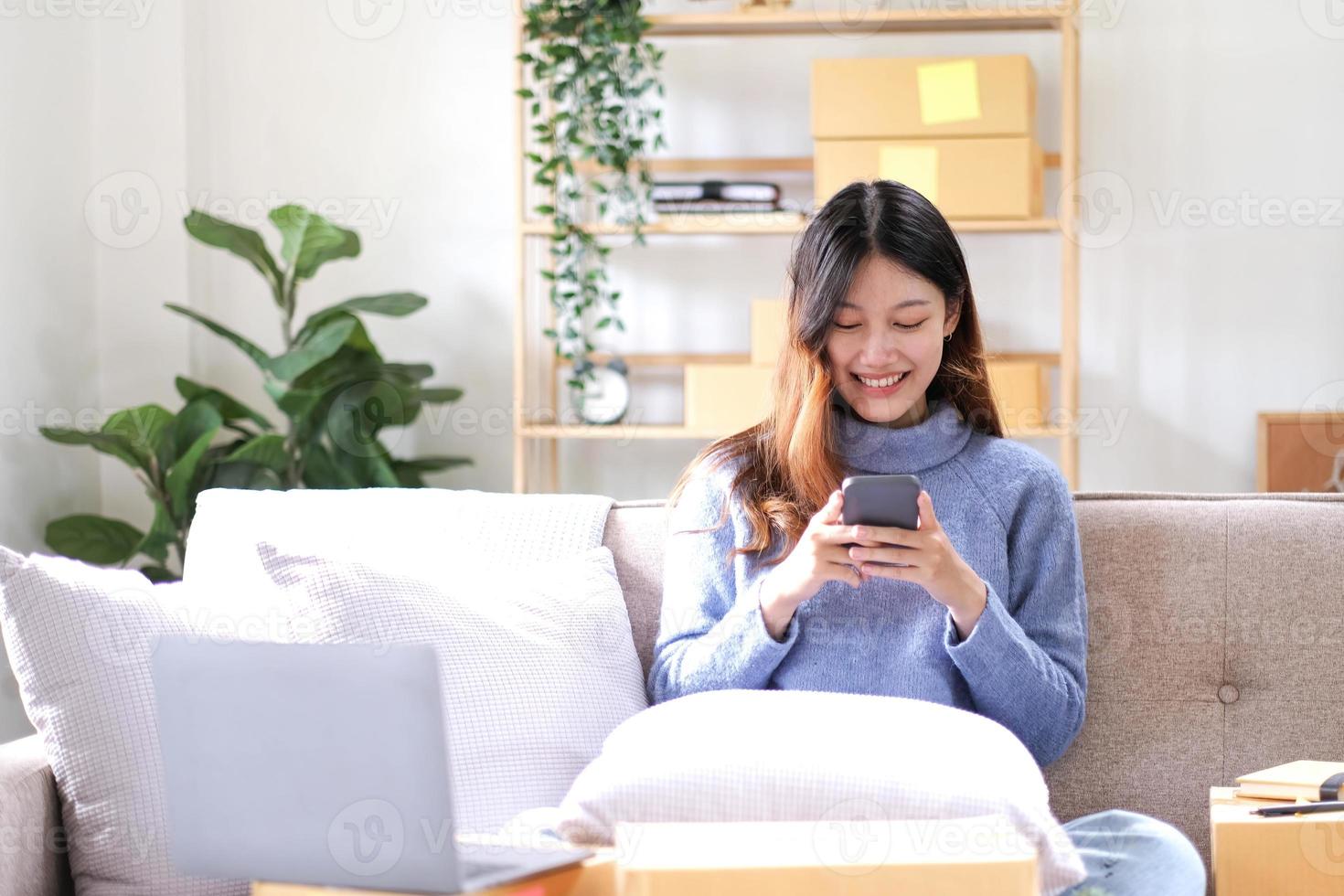 Aziatisch bedrijf vrouw Aan sofa gebruik makend van een laptop computer controle klant bestellen online Verzending dozen Bij huis. beginnend mkb klein bedrijf ondernemer freelancer. online bedrijf, mkb werk huis concept. foto