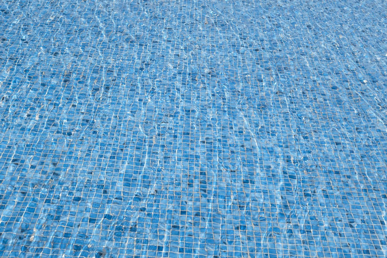 de wind maakt de water rimpeling. Doorzichtig oppervlakte water abstract achtergrond. blauw zwemmen zwembad reflecterend de zon golfde. patroon van de bodem van de zwembad gemaakt van golfde mozaïek- keramisch blauw tegels. foto