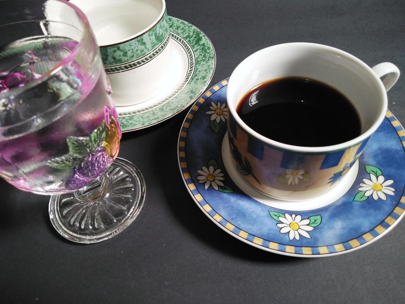 theekopje, koffie kop en transparant fruit gevormde glas gevulde met mineraal water Aan een zwart achtergrond. foto