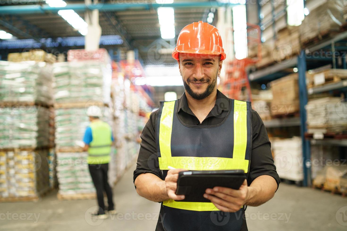 professioneel manager Mens werknemer gebruik makend van tablet controleren voorraad werken Bij magazijn. arbeider vervelend hoog zichtbaarheid kleding en een moeilijk hoed, helm en controle en tellen omhoog goederen of dozen voor levering. foto