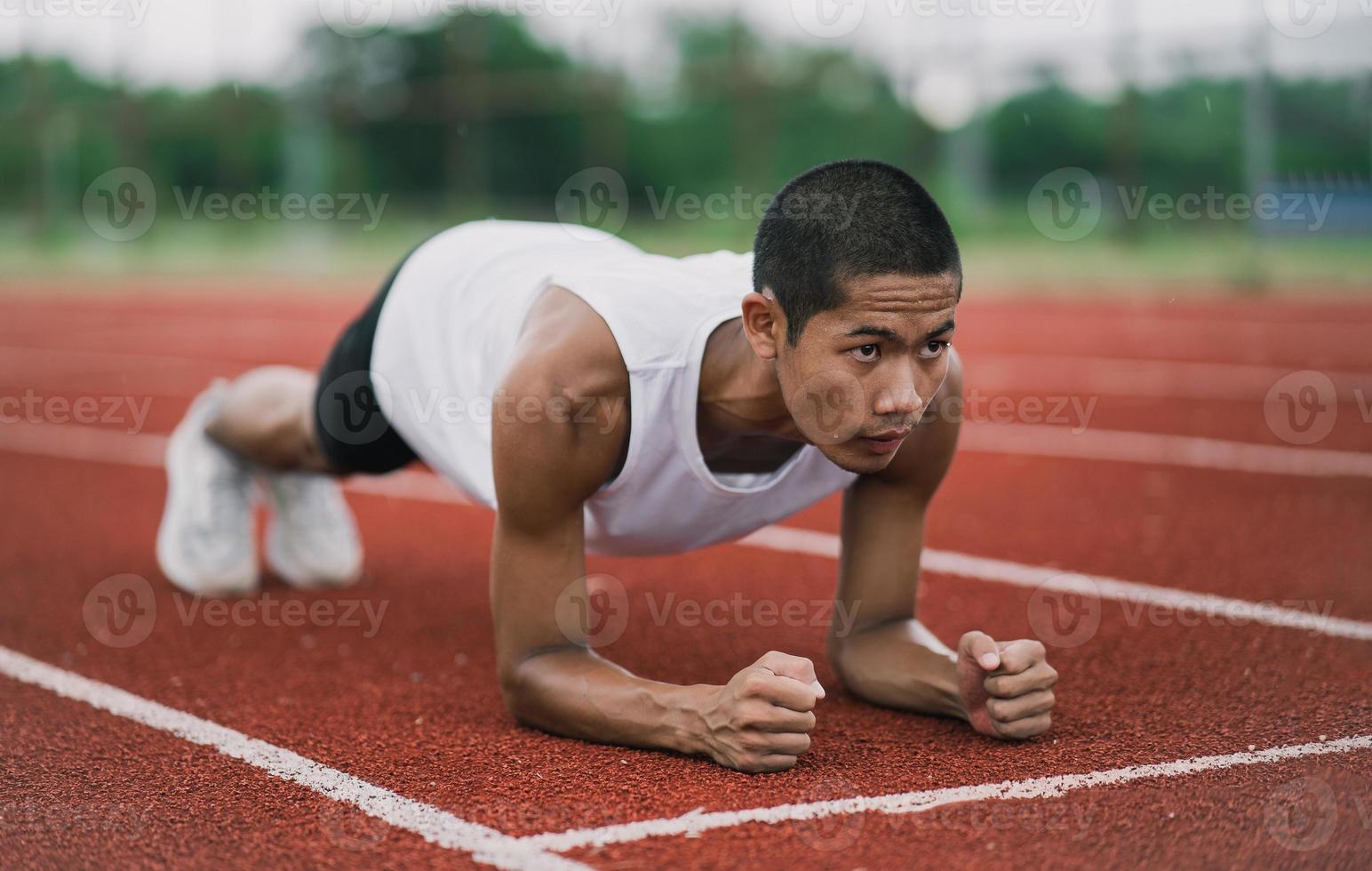 atleten sport Mens loper vervelend wit sportkleding naar planken uitrekken en warm omhoog voordat beoefenen Aan een rennen bijhouden Bij een stadion. loper sport concept. foto