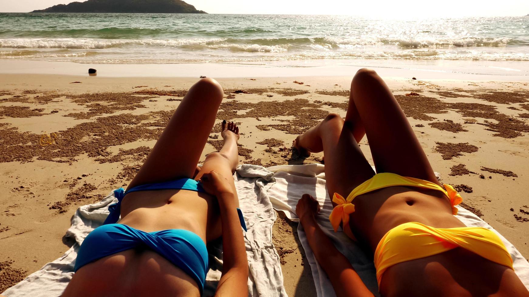 twee sexy Dames aan het liegen naar beneden samen Aan de strand. foto