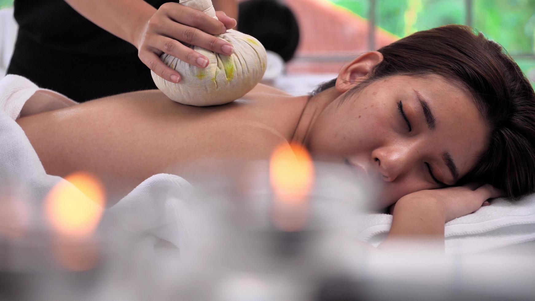 jong Aziatisch vrouw krijgen ontspannende gedurende therapeut zetten kruiden spa bal Aan de terug en massage in spa salon. foto