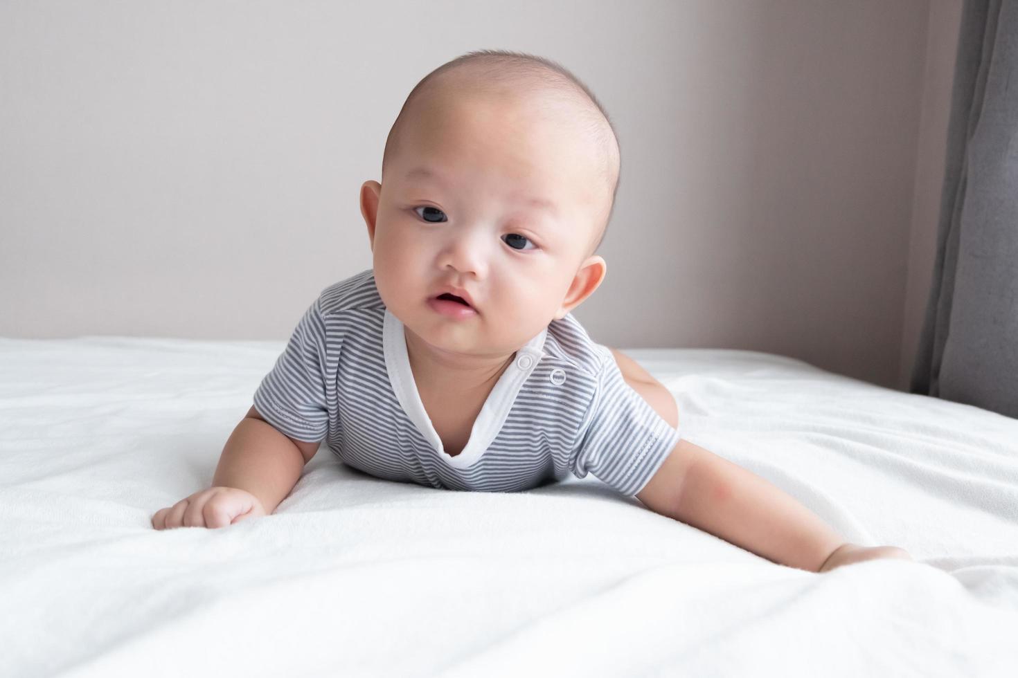 portret baby in een gestreept shirt, voorkant visie, kruipen Aan een wit matras foto