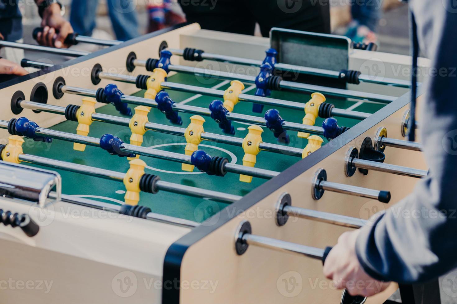 bijgesneden afbeelding van actieve mensen die kicker of tafelvoetbal spelen, succes willen behalen en winnen, de voorkeur geven aan sportgames. voetbaltafel met gele en blauwe plastic spelers foto