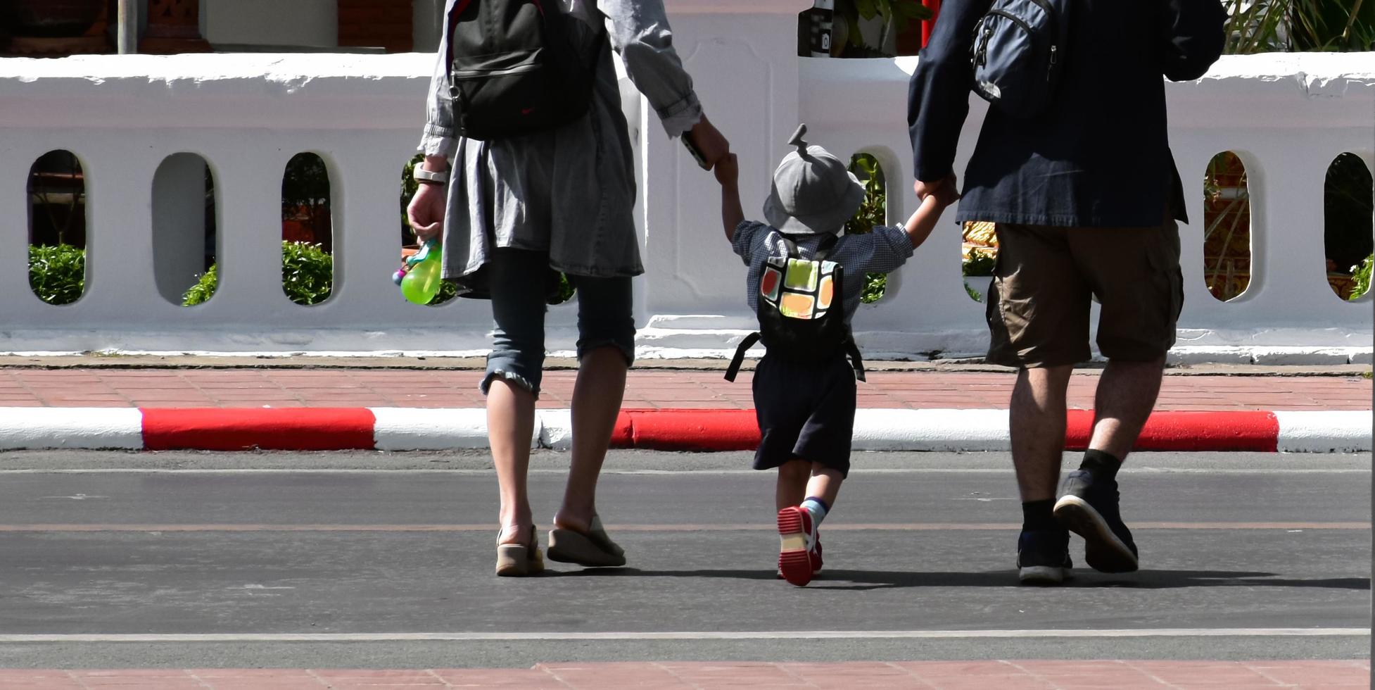 Aziatisch ouders familie reizigers houden hun zoon armen wanneer ze liep kruis de straat. foto
