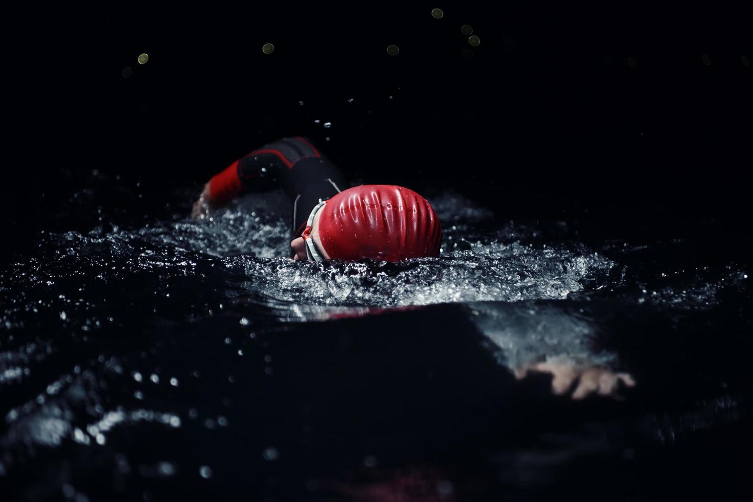 triatlonatleet die in donkere nacht zwemt die wetsuit draagt foto