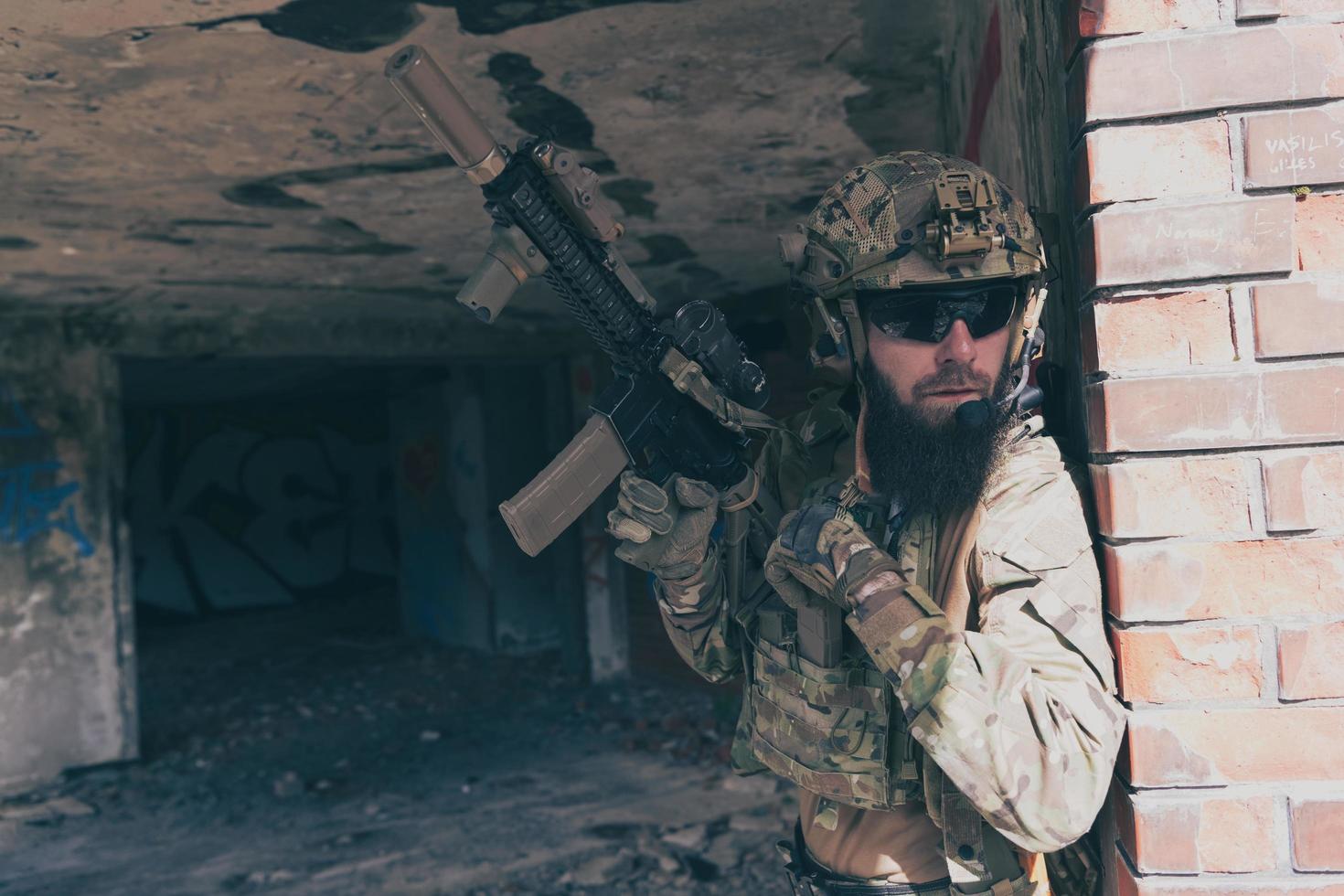 een gebaard soldaat in speciaal krachten uniform in gevaarlijk leger missie, opnieuw archiveren zijn wapen terwijl schuilplaats van de muur. selectief focus foto