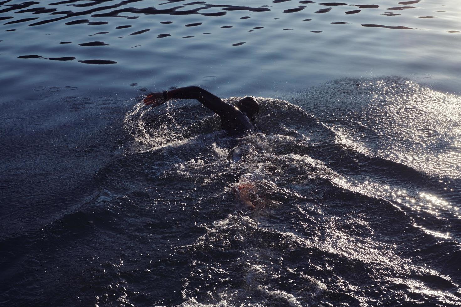 triatlonatleet die op meer in zonsopgang zwemt die wetsuit draagt foto