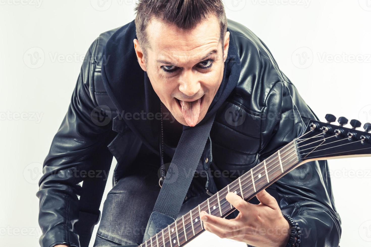 rebels musicus plakken uit tong terwijl spelen elektrisch gitaar. foto