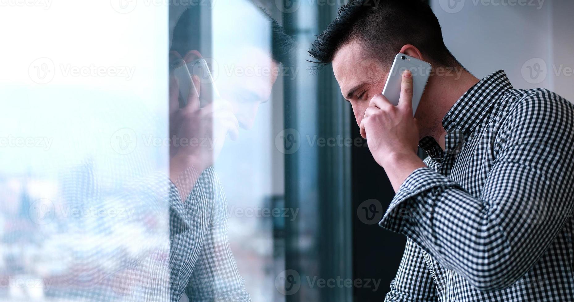 bedrijf Mens pratend Aan cel telefoon, op zoek uit kantoor venster foto