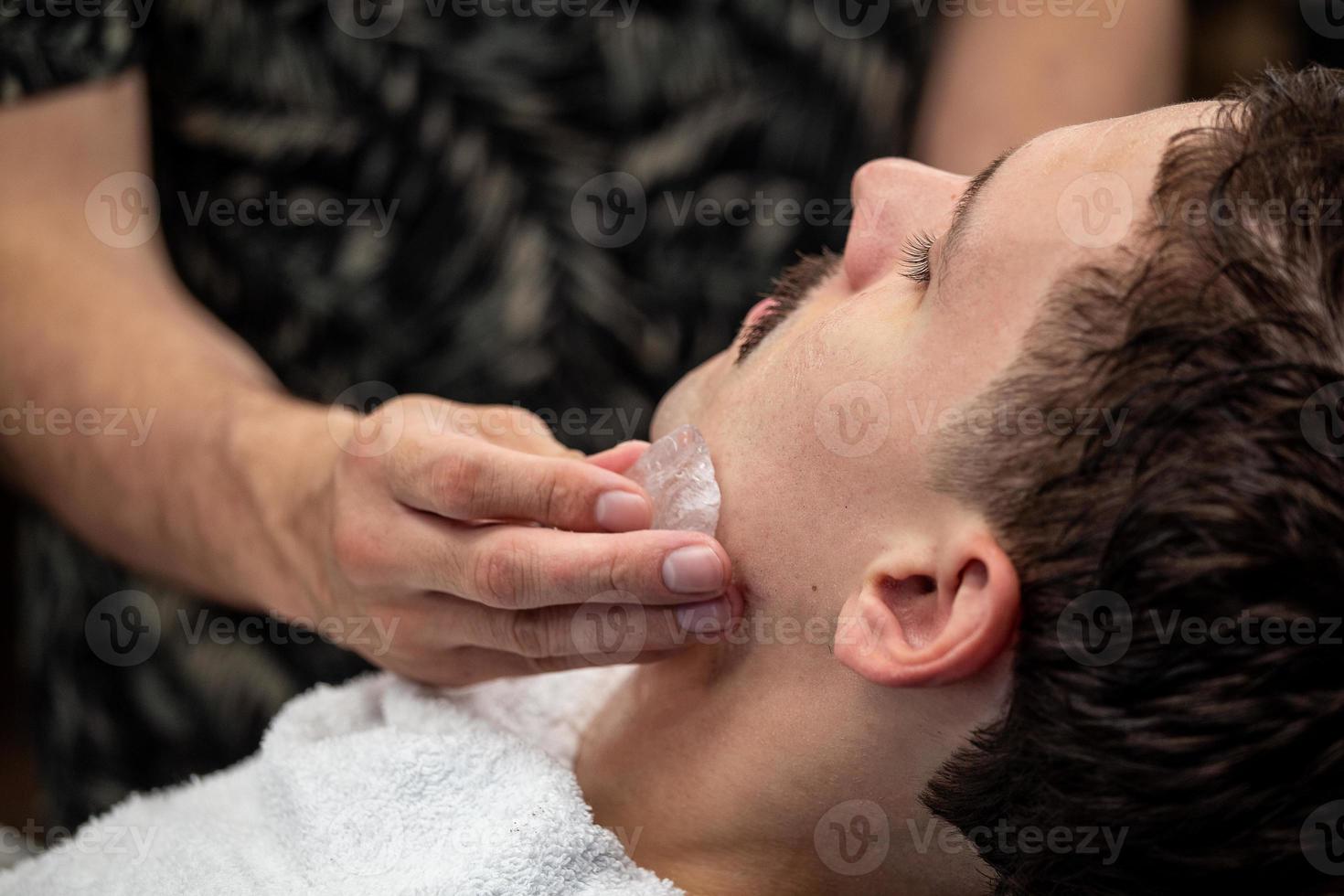 kapper sluitend mans met aluin steen. traditioneel ritueel van na scheren de baard met aluin steen. krijgen zijn gezicht gewreven met aluin steen na scheren kapper winkel 11668387 Stockfoto