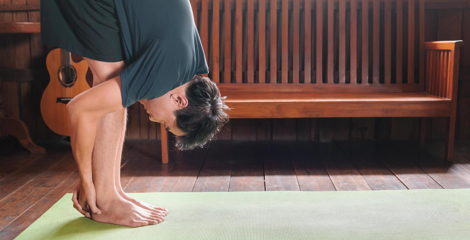 sportief Aziatisch Mens in zwart is aan het doen yoga terwijl oefenen Aan yoga mat Bij huis met houten verdieping.man yoga praktijk houding opleiding gezond leven concept foto