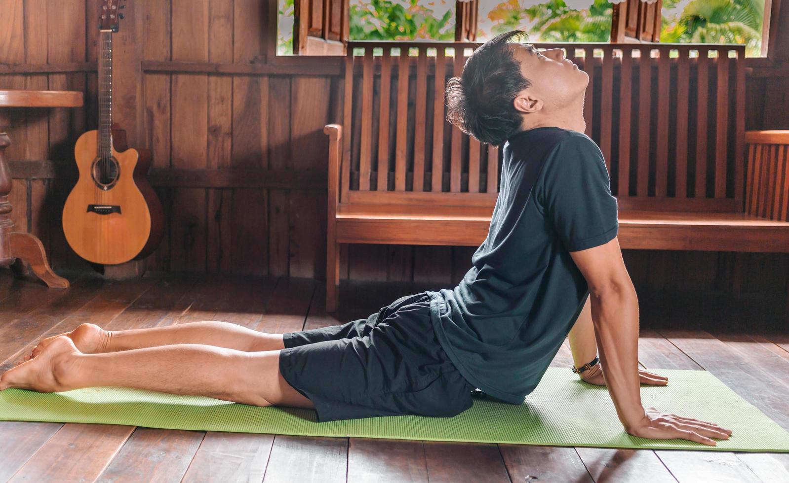 sportief Aziatisch Mens in zwart is aan het doen yoga terwijl oefenen Aan yoga mat Bij huis met houten verdieping.man yoga praktijk houding opleiding gezond leven concept foto