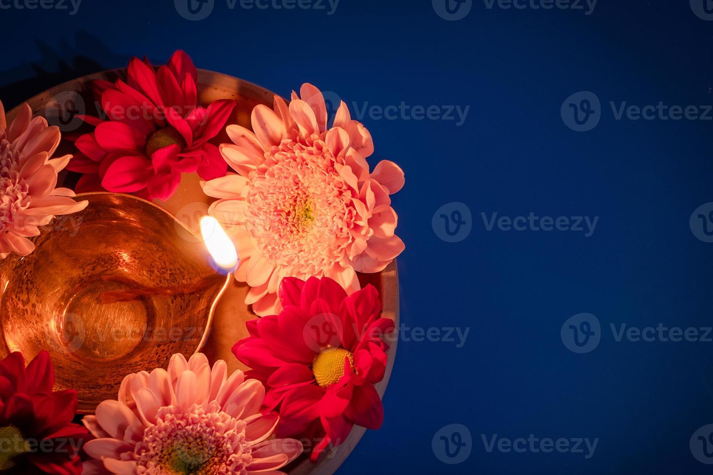 gelukkig divali. vieren de Indisch festival van licht. traditioneel diya olie lampen en rood bloemen Aan blauw achtergrond foto