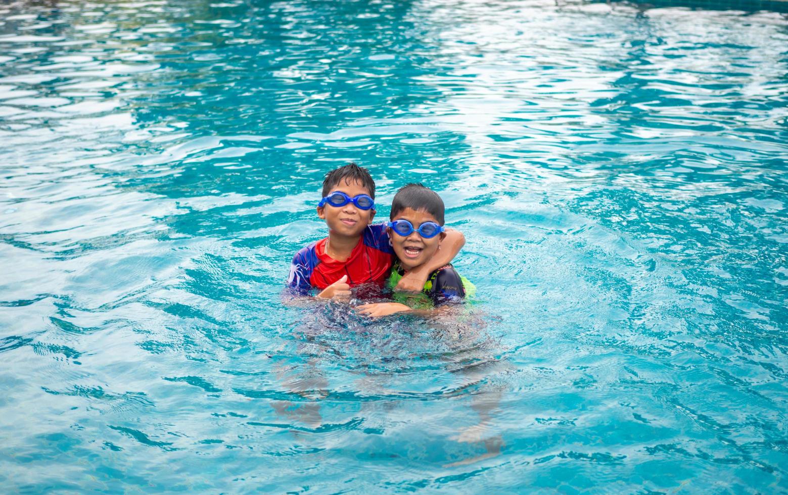 broers slijtage een zwempak en stofbril. glimlach en genieten spelen in de water in de blauw zwembad foto