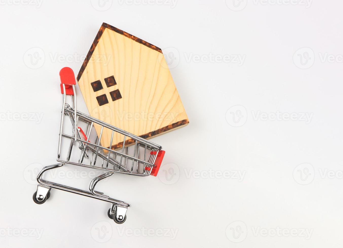 vlak lay-out van houten huis model- in boodschappen doen trolley Aan wit achtergrond, huis aankoop concept. foto