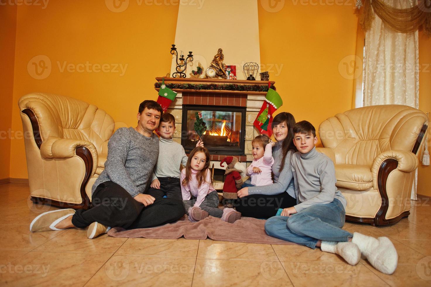 gelukkige jonge grote familie thuis bij een open haard in warme woonkamer op winterdag. foto