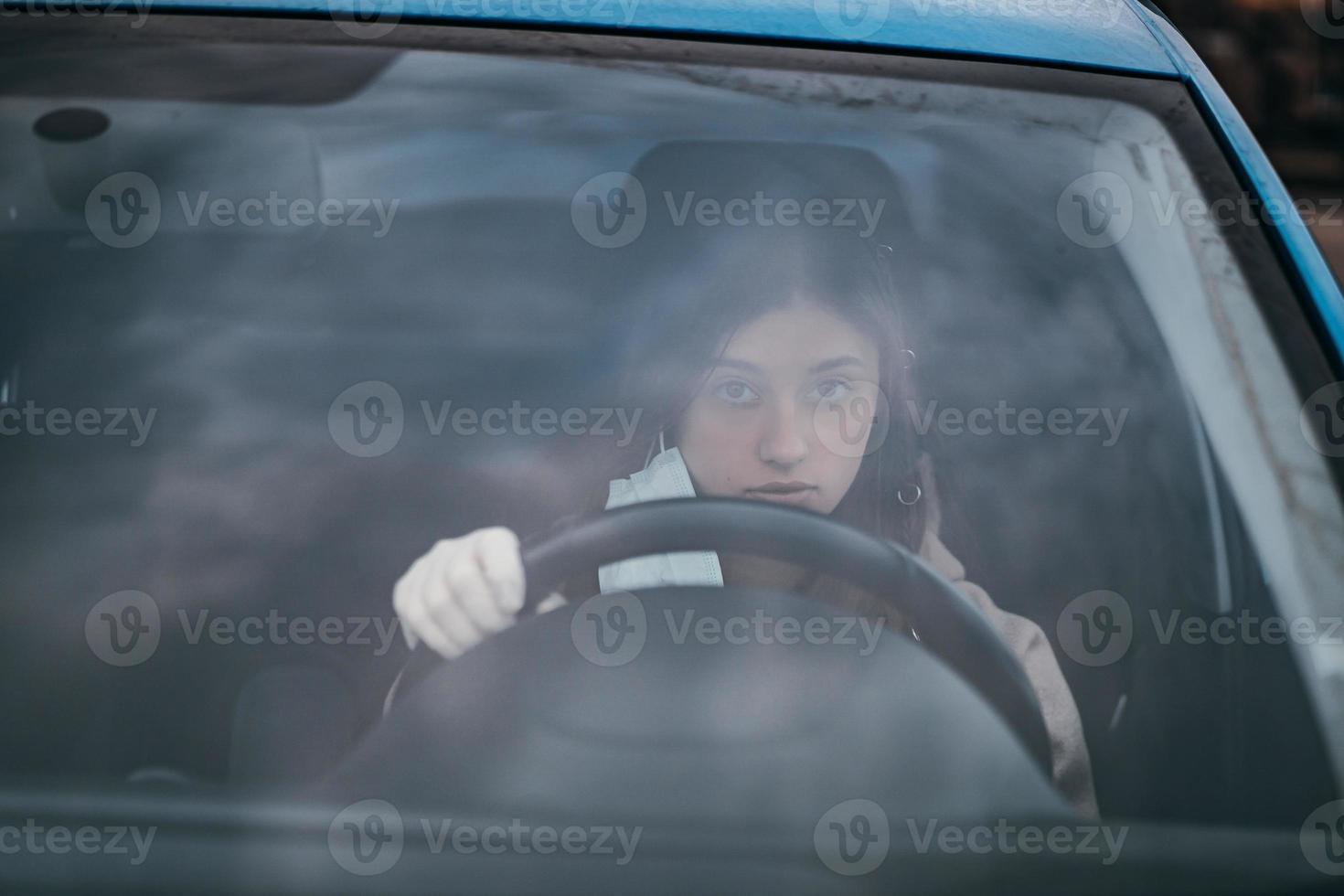 jong vrouw in een masker en handschoenen het rijden een auto. foto