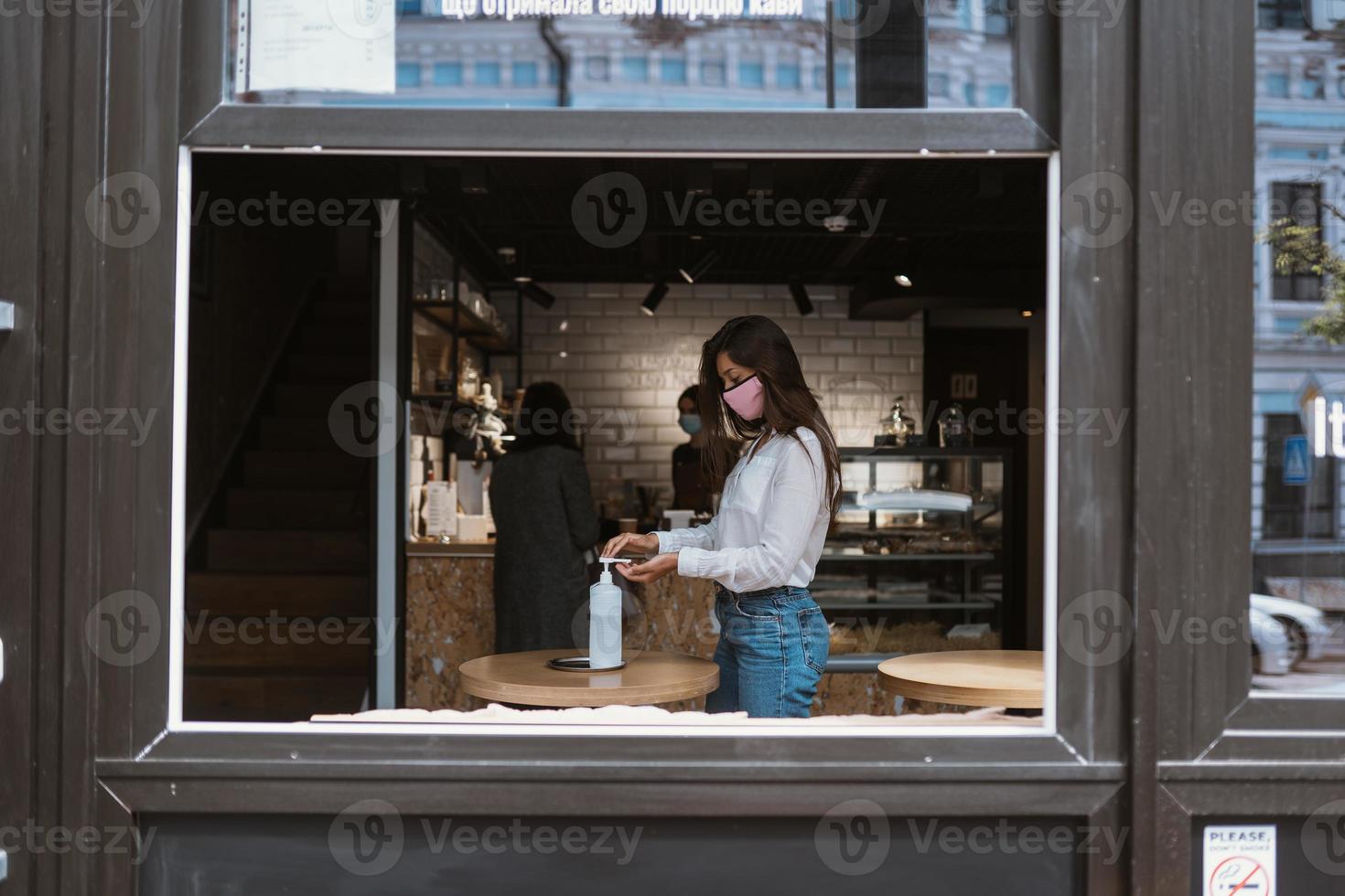 vrouw gebruik makend van ontsmettingsmiddel gel reinigt handen van coronavirus virus Bij cafe. foto