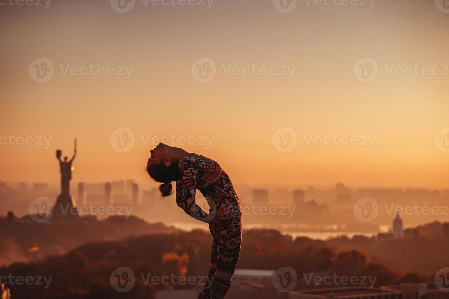 vrouw aan het doen yoga Aan de dak van een wolkenkrabber in groot stad. foto