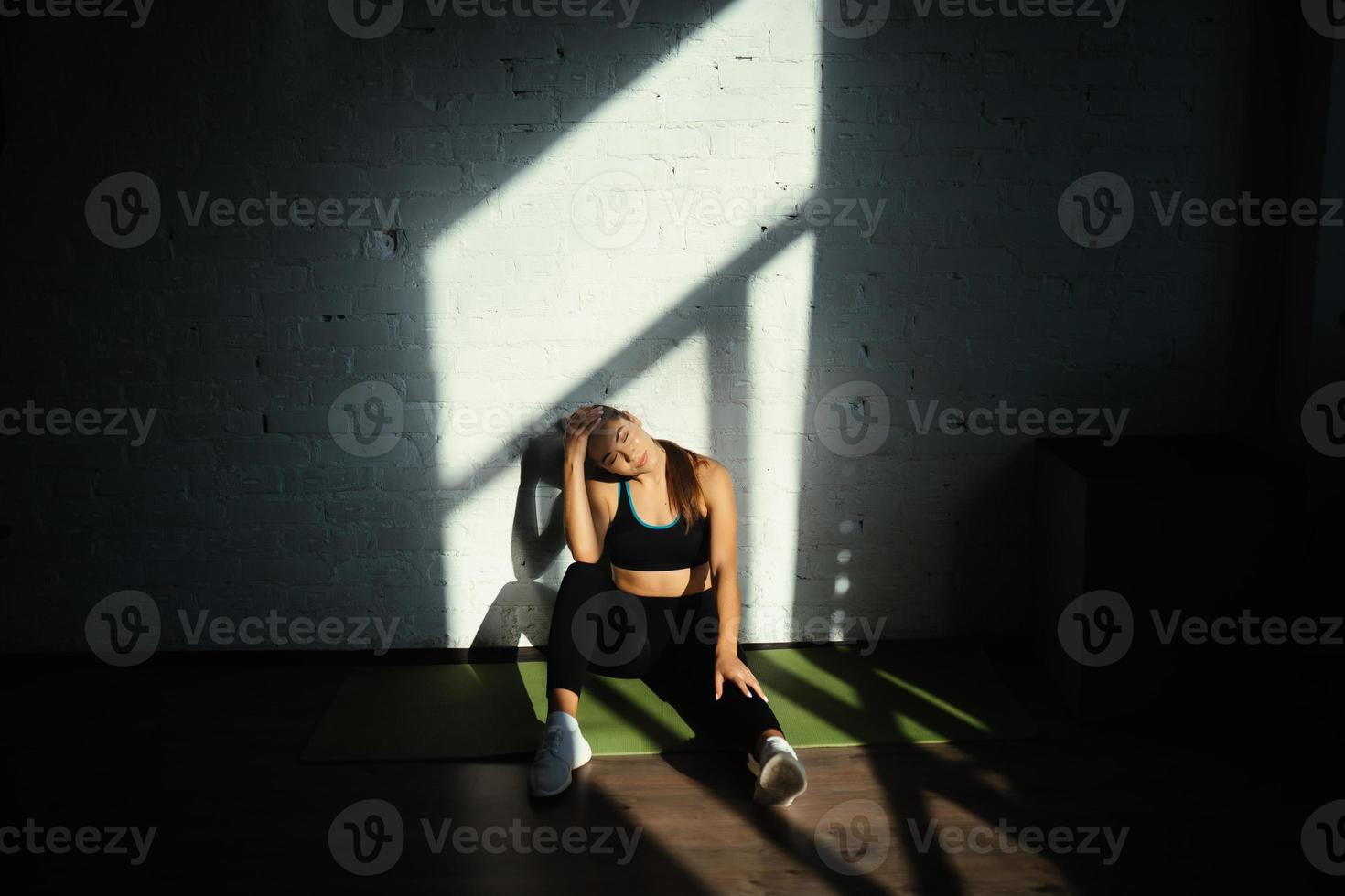 fit vrouw resting na huis training, zittend Aan mat foto