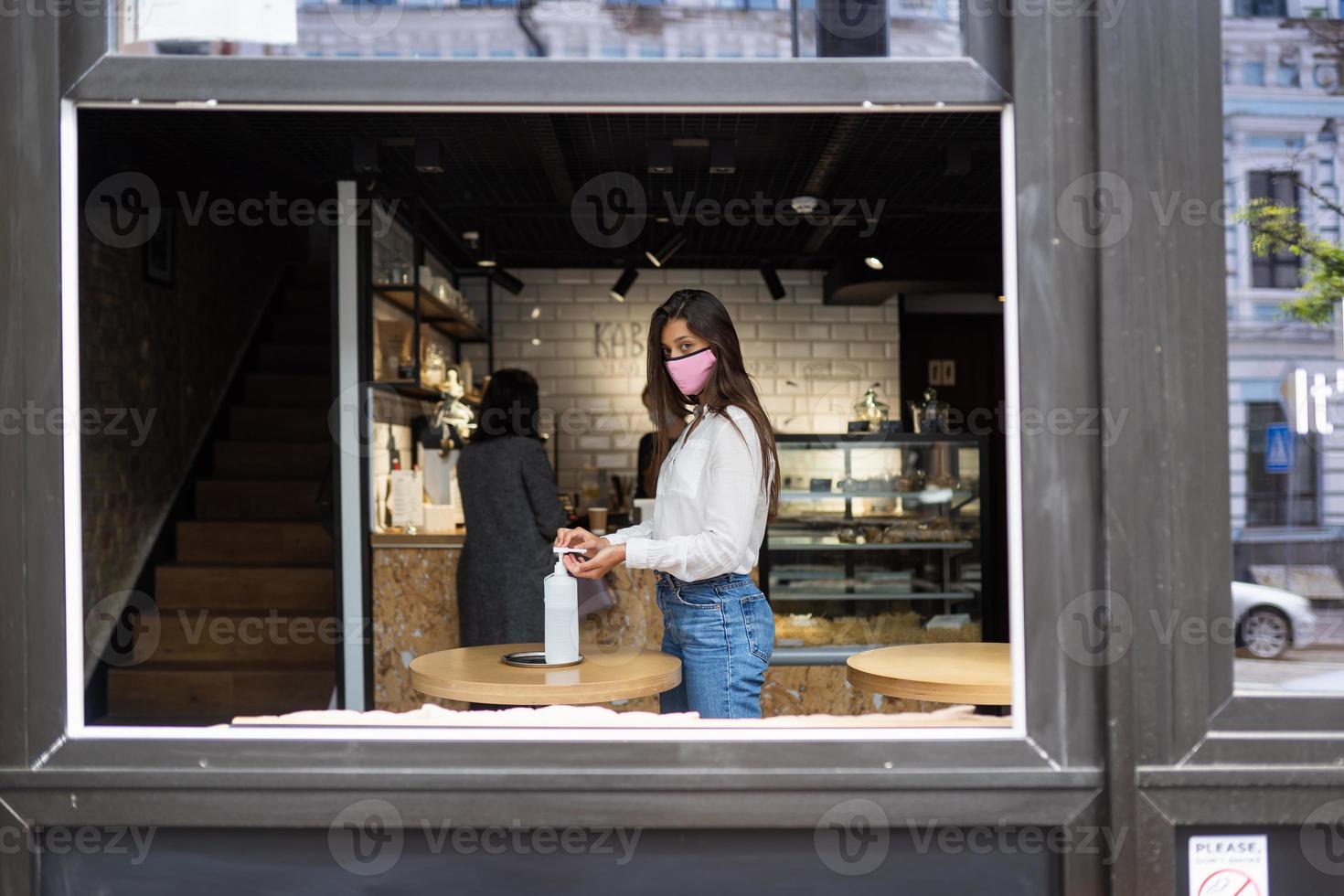 vrouw gebruik makend van ontsmettingsmiddel gel reinigt handen van coronavirus virus Bij cafe. foto