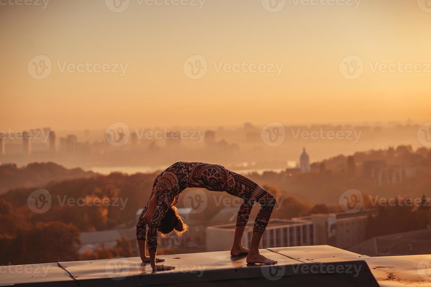 vrouw aan het doen yoga Aan de dak van een wolkenkrabber in groot stad. foto