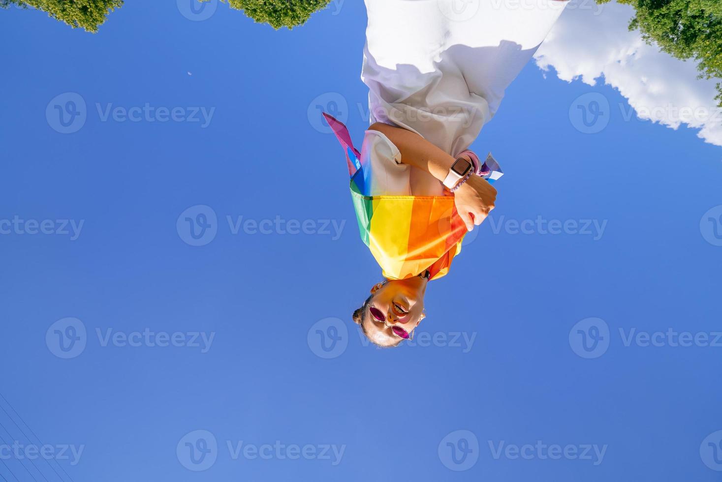 een jong vrouw ontwikkelt een regenboog vlag tegen de lucht foto