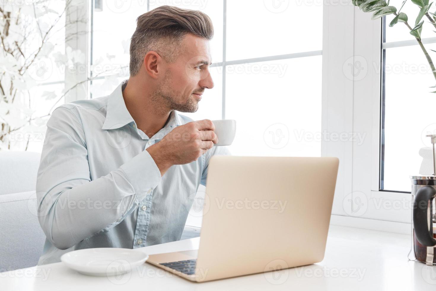 knappe zakenman die met laptop werkt en kop koffie in koffie heeft foto