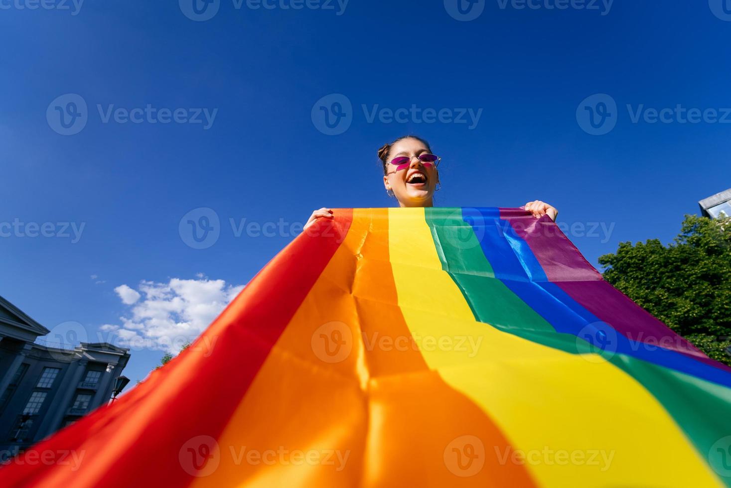 een jong vrouw ontwikkelt een regenboog vlag tegen de lucht foto