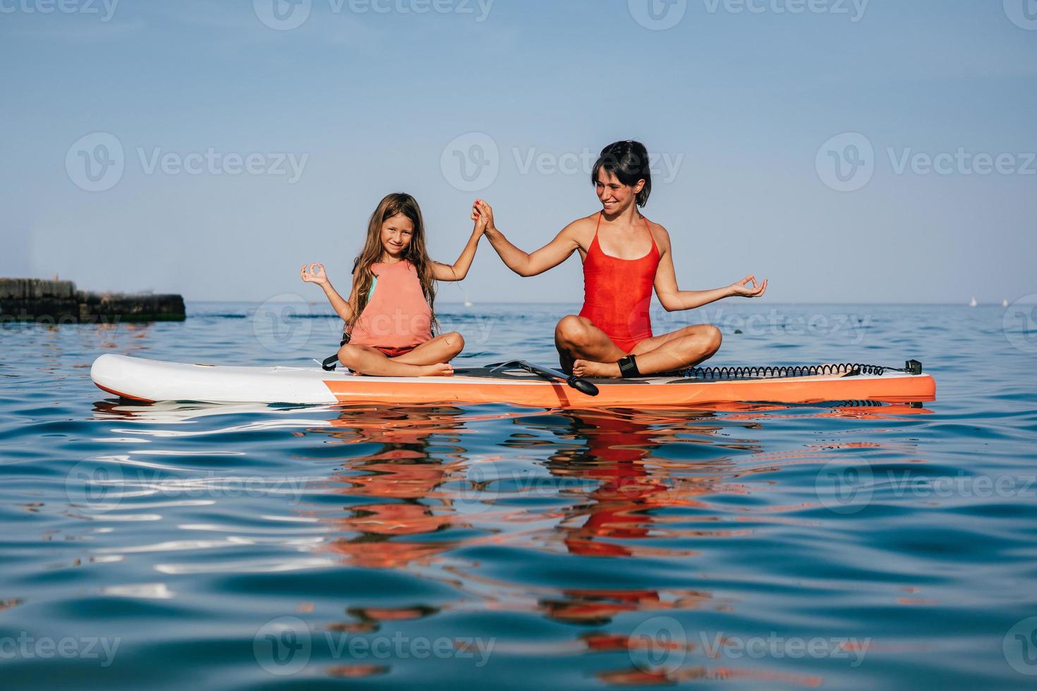 mam en weinig dochter aan het doen yoga Aan de peddelen bord foto