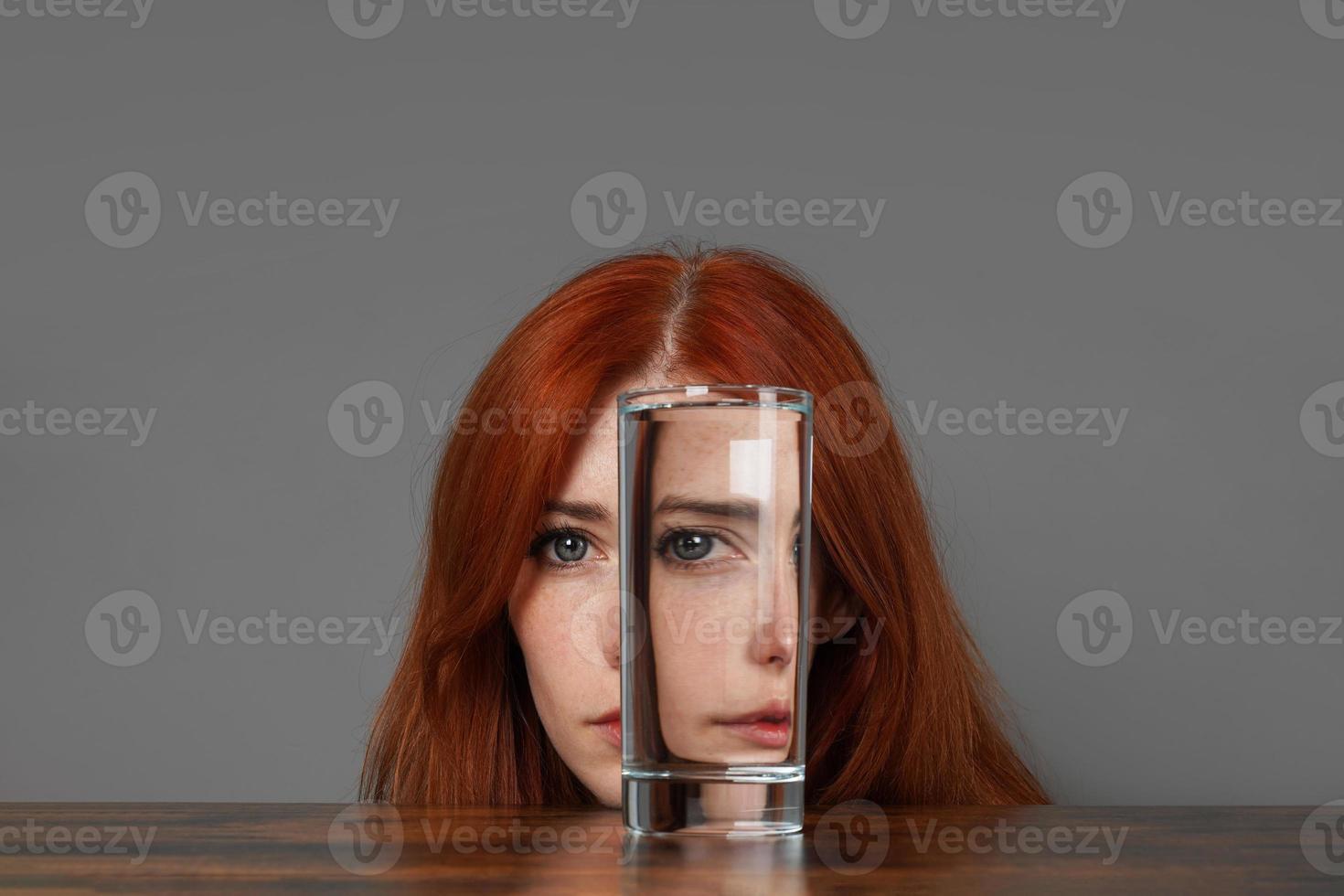 vervormd gezicht van vrouw op zoek door glas van water foto