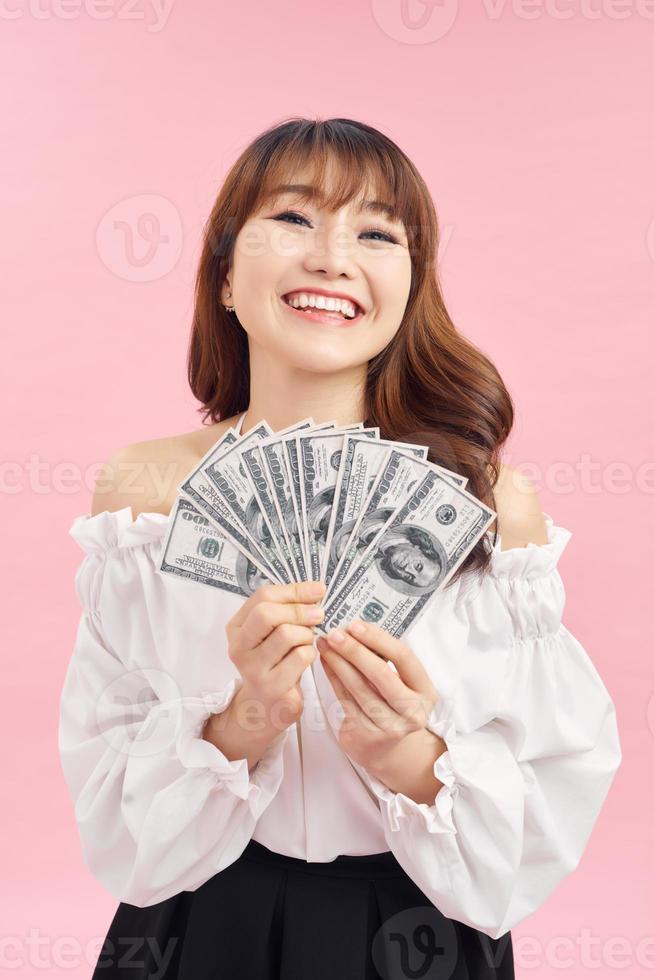 aantrekkelijk opgewonden jong meisje vervelend gewoontjes kleding staand geïsoleerd over- roze achtergrond, tonen geld bankbiljetten, vieren foto