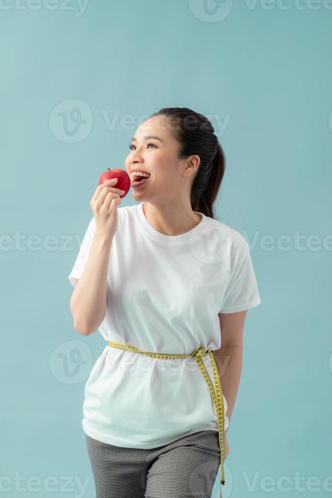 mooi sportief vrouw gebruik makend van plakband meten aan het eten appel fruit over- blauw achtergrond foto