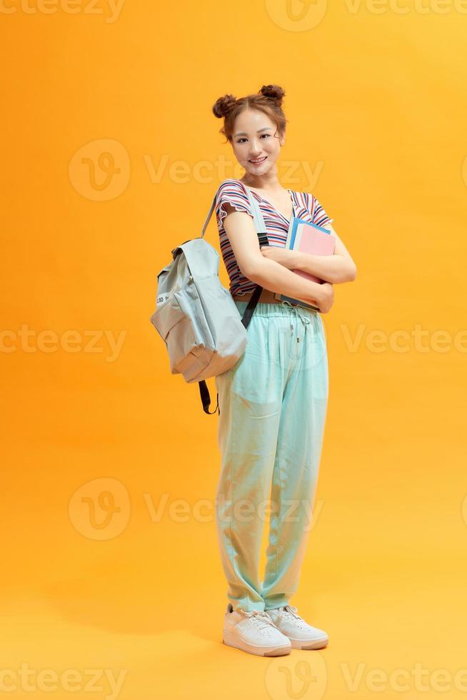 vol lengte portret van een vrouw leerling met een rugzak en boeken geïsoleerd Aan geel achtergrond foto