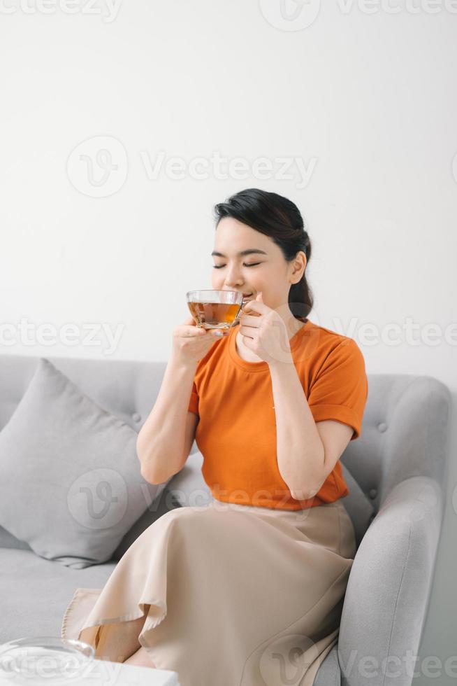 mooi jong vrouw ontspannende Aan sofa met laptop en een kop van thee in huis foto