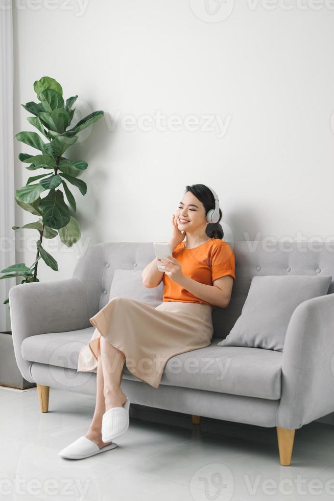 sereen jong vrouw resting Aan sofa vervelend gewoontjes huis kleren draadloze hoofdtelefoons genieten weekend vrij tijd foto