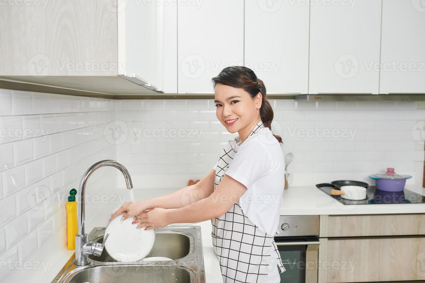 jong vrouw met schort het wassen gerechten in modern keuken foto
