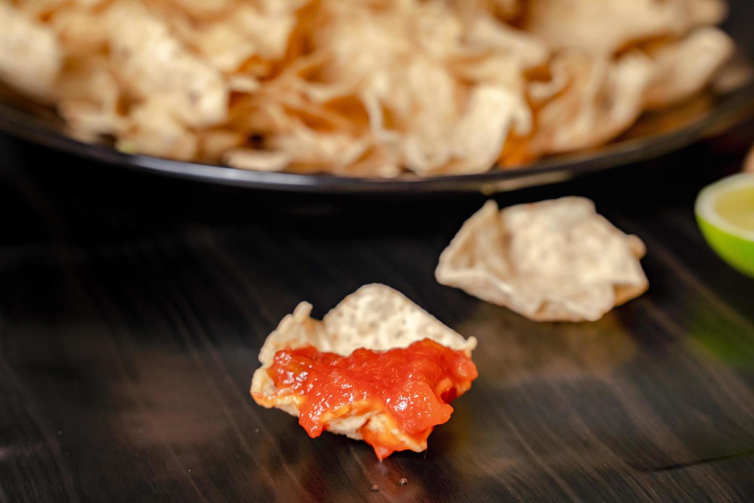 dichtbij omhoog hand- houden spaander dip tomaat salsa met bord met taco, nacho's chips en tomaat duik. pittig nacho's Aan rustiek houten achtergrond foto