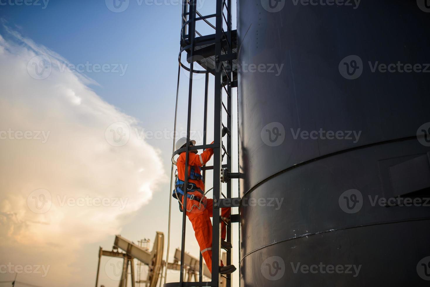Mens werken in olie tuigage of olie veld- plaats, beklimmen olie tank voor werken in avond tijd met verrassing of zonsondergang. foto