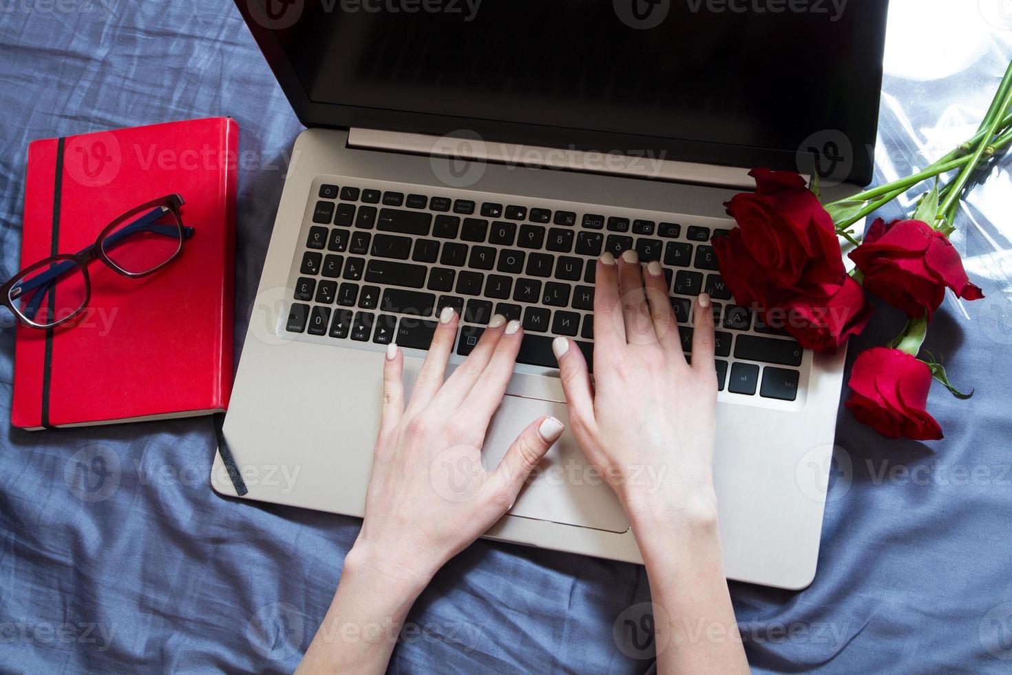 handen, computertoetsenbord, bed bovenaanzicht. achtergrond op de werkplek, thuiswerken, notitieblok en bloemen foto
