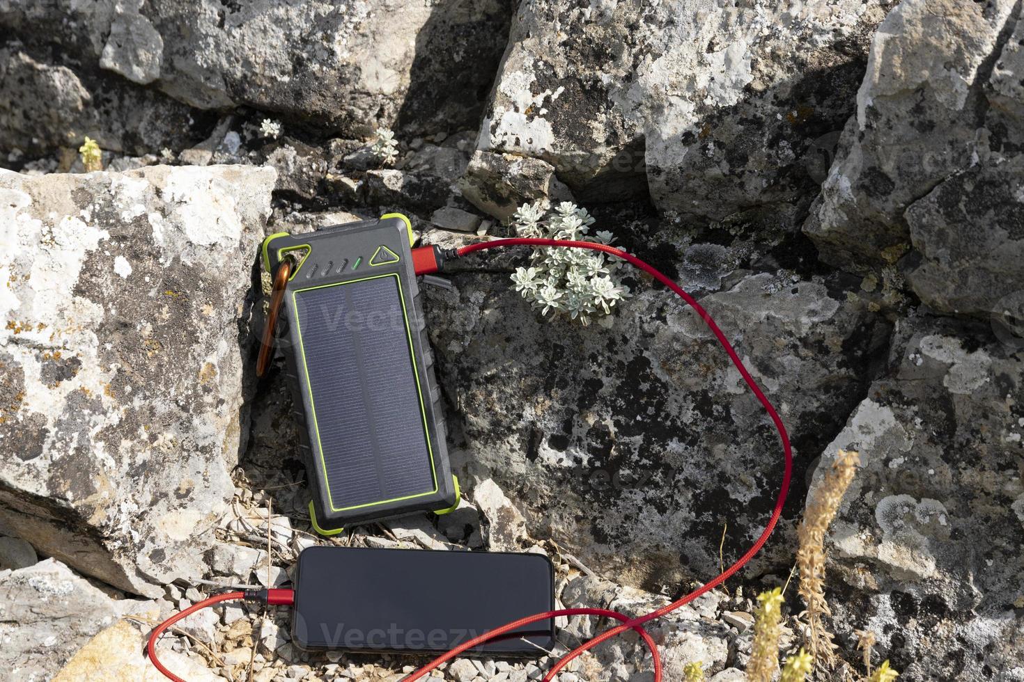 de smartphone is opgeladen van een portable oplader Aan een zonne- paneel terwijl hiking. foto