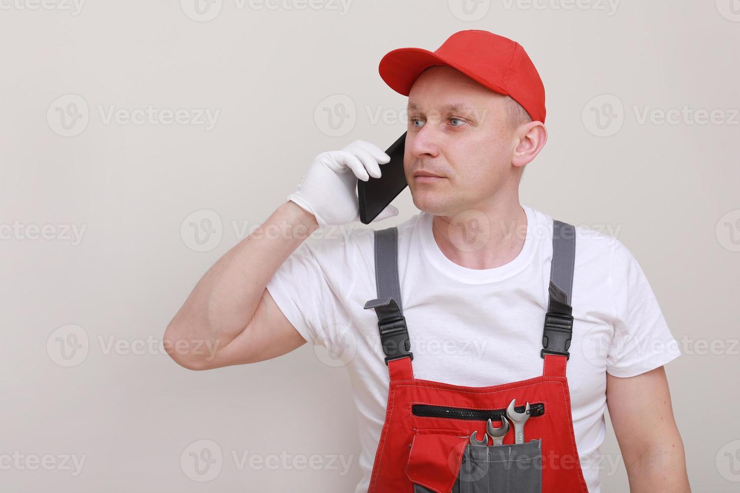 bouw mannetje arbeider in rood werken het formulier en pet met mobiele telefoon in hand- en communiceert met klanten geïsoleerd Aan wit achtergrond. van de onderhoud levering is een carrière foto