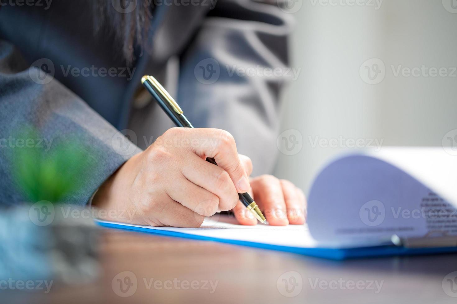 werkplaats detailopname persoon professioneel zakenvrouw zittend Bij bureau houden pen ondertekening of handtekening contract papier. werknemer vrouw schrijven overeenkomst document Aan papierwerk het formulier zakelijke Bij werk kantoor foto