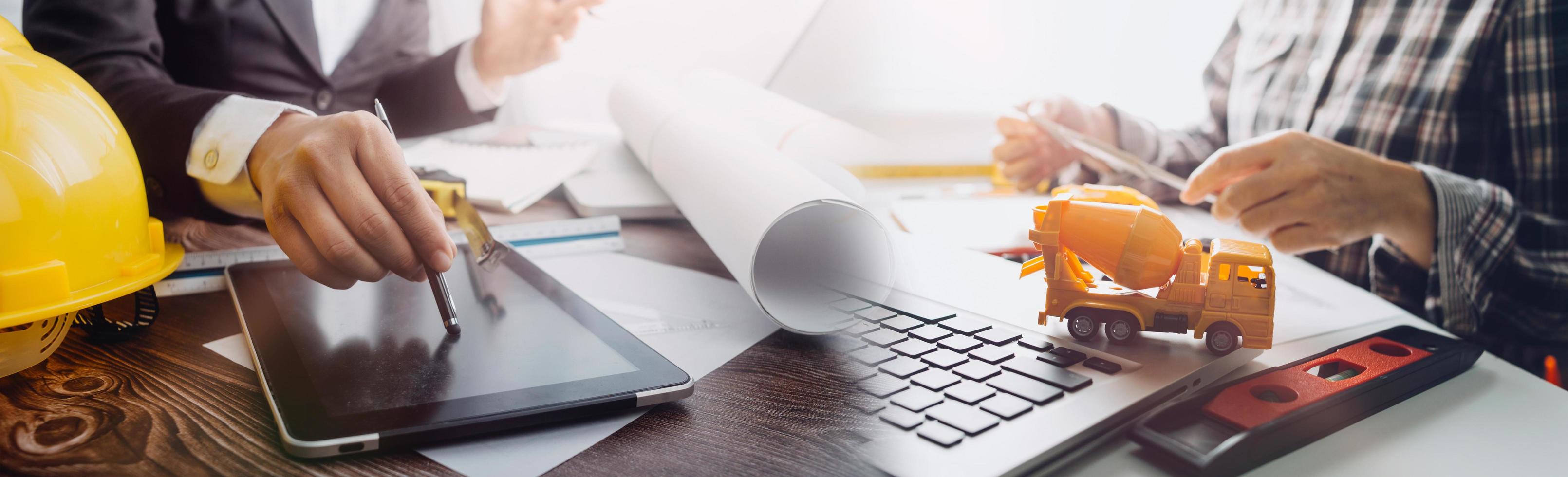 twee collega's bespreken gegevens werken en tablet, laptop met op architectonisch project op bouwplaats aan balie in kantoor foto