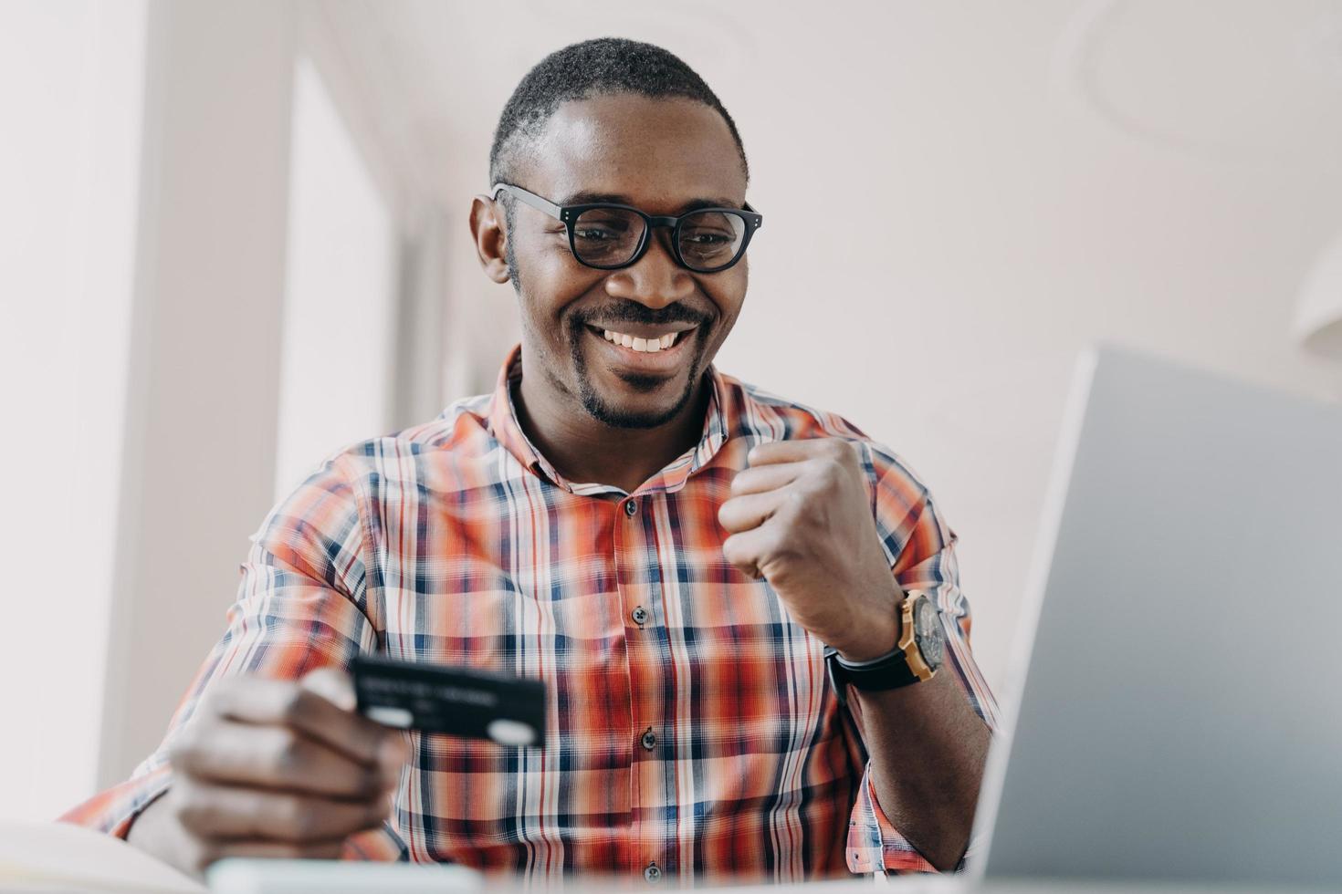 Afrikaanse Amerikaans Mens gebruik makend van online bank onderhoud Bij laptop, Holding credit kaart maakt Ja gebaar foto